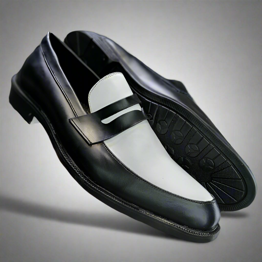 Black and white loafer shoe held by a hand with a blurred background of shoes on shelves.