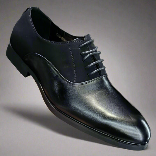 Black dress shoe held by a hand against a blurred indoor background