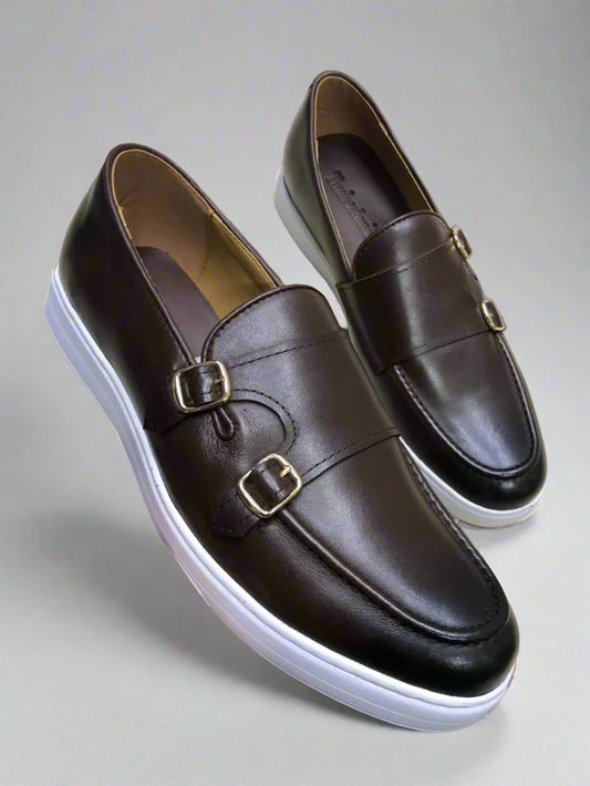 Brown leather shoes with gold buckles held by a hand on a light background