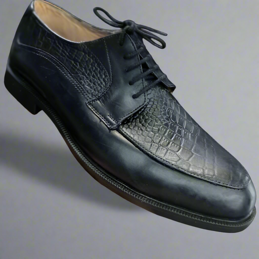 Black leather dress shoe with textured toe cap held by a hand on a white background