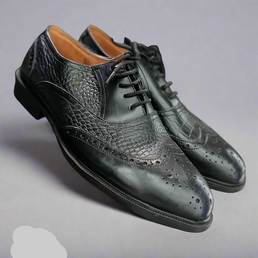 Black leather dress shoes with detailed design held by a person wearing black socks.