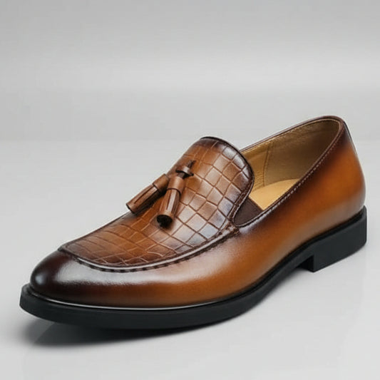 Brown leather shoe with a tassel held by a hand against a cluttered background