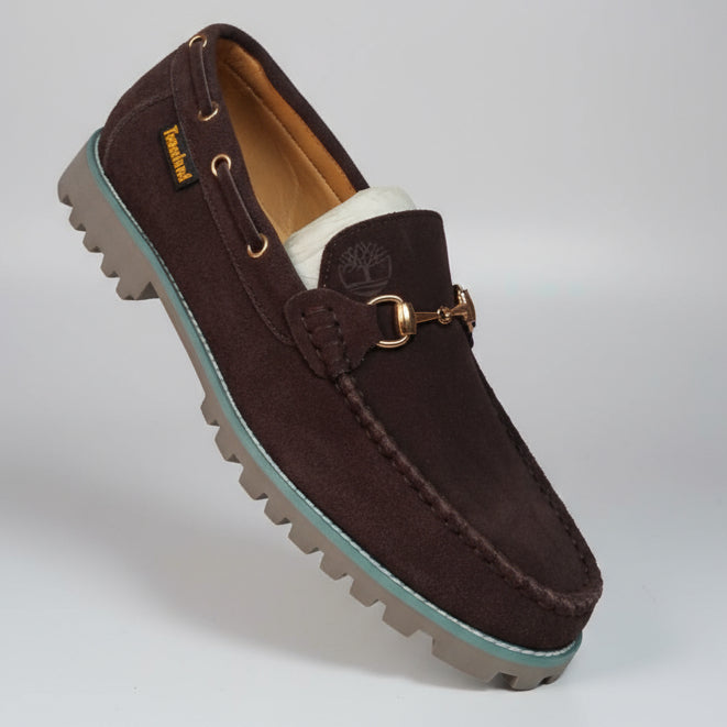 Brown loafer shoe held by a hand with a blurred background