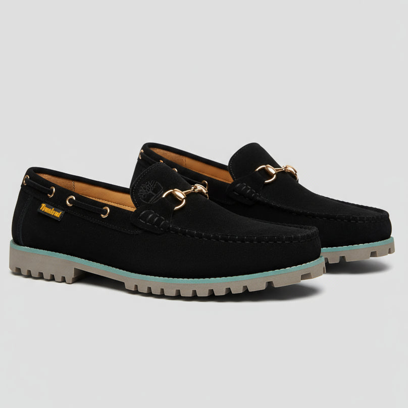 Black loafer shoe held by a hand with a blurred background