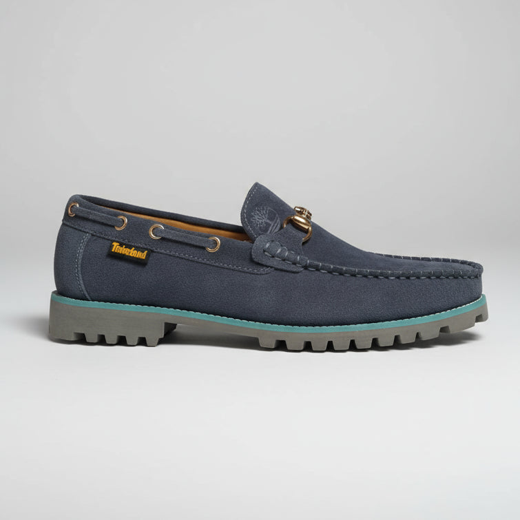 grey suede loafer held by a hand with a blurred background of shoes.