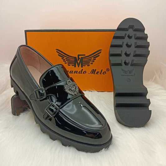 Black shiny loafers with a brand box on a white background, featuring the brand logo.