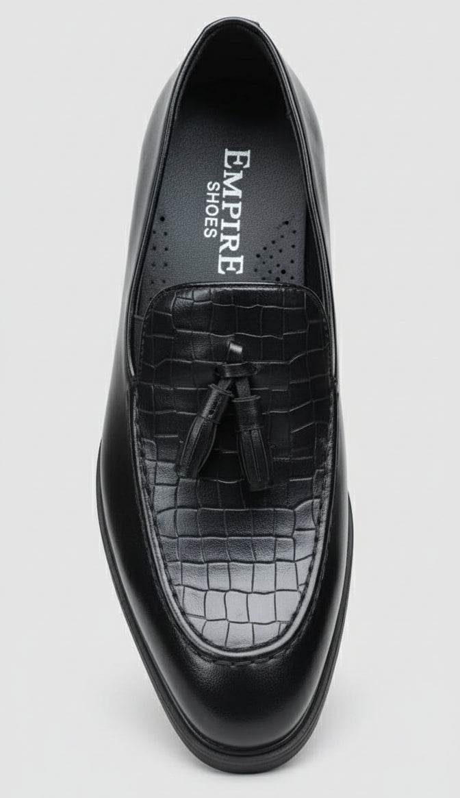 Black leather shoe with tassel held by a hand against a cluttered background