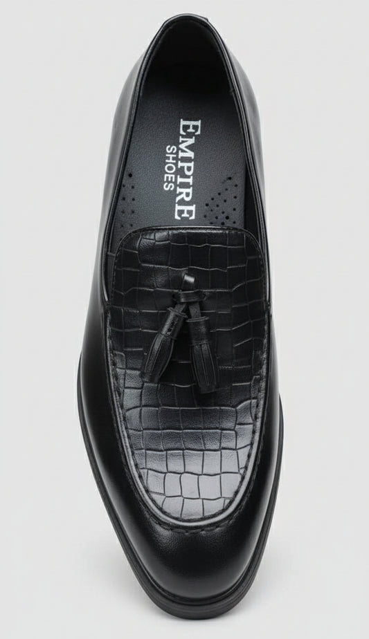 Black leather shoe with tassel held by a hand against a cluttered background