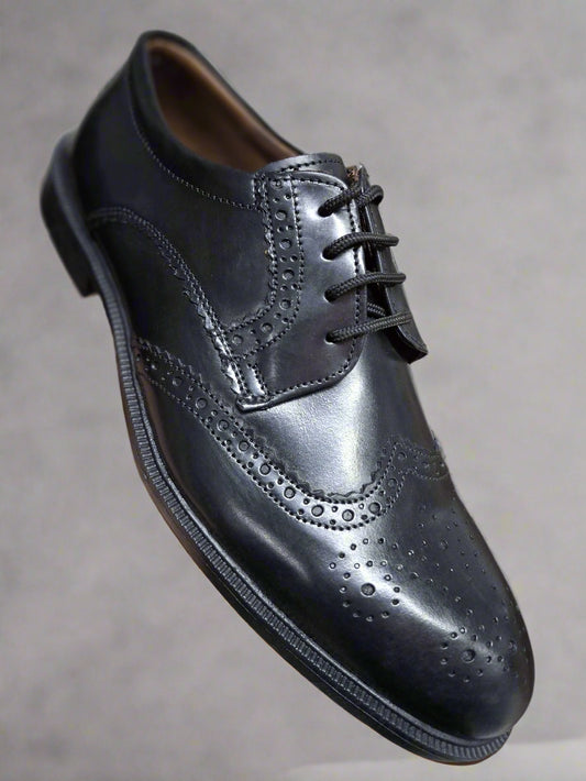 Black leather dress shoe held by a hand against a neutral background